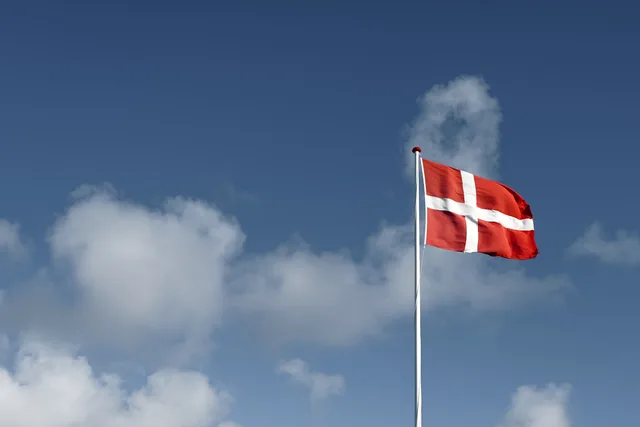 A beautiful view of the Danish flag waving high against a vivid blue sky with fluffy clouds. Geografisk markedsafgrænsning med CVR og Danmarks Statistik
