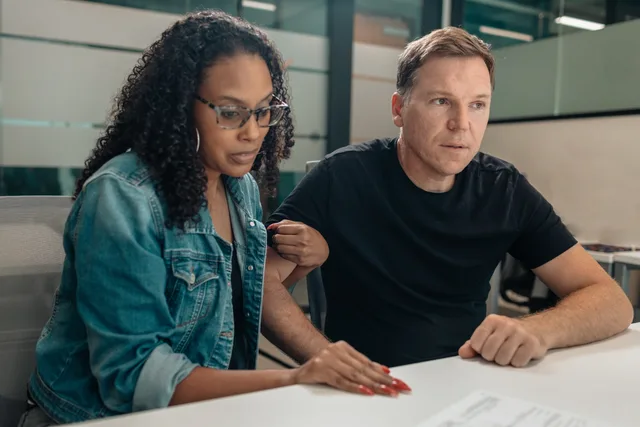 A couple closely examining paperwork in a modern office space. Focused and serious mood. Teknologiadoption i danske virksomheder: Behov, risiko og modenhed